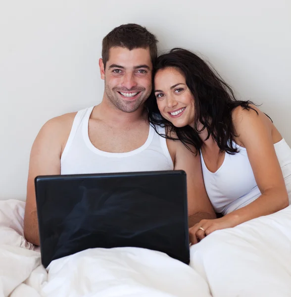 Casal brilhante usando um laptop em uma cama — Fotografia de Stock