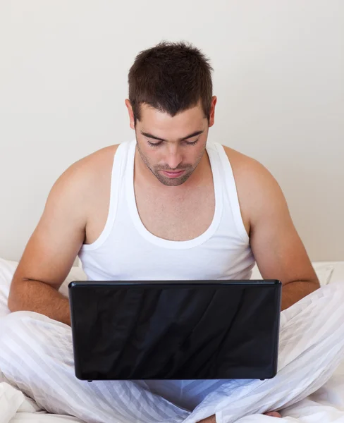 Серьезный человек, использующий ноутбук в своей спальне — стоковое фото