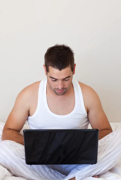 Серйозний чоловік використовує ноутбук у своїй спальні — стокове фото