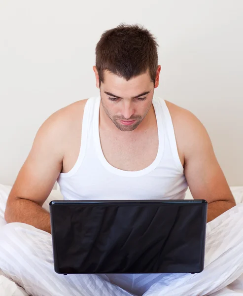 Uomo serio che utilizza un computer portatile nella sua camera da letto — Foto Stock