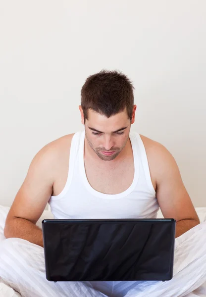 Genç adam onun yatak odasında bir dizüstü bilgisayar kullanarak — Stok fotoğraf