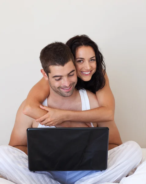 Casal encantador usando um laptop sentado em uma cama — Fotografia de Stock