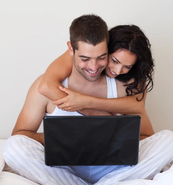 Прекрасная пара, сидящая на кровати с ноутбуком — стоковое фото