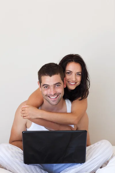 Mooie paar met behulp van een laptop zittend op een bed — Stockfoto