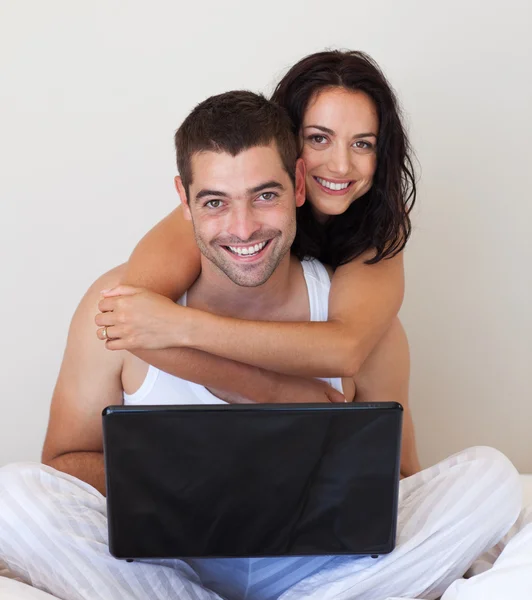 Casal alegre usando um laptop sentado em uma cama — Fotografia de Stock