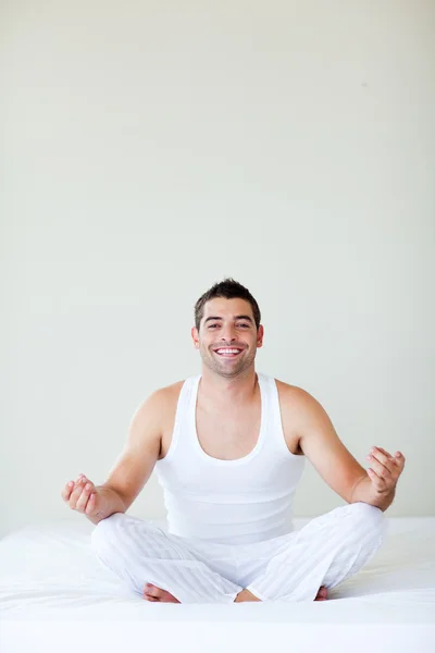Homem sorridente sentado na cama meditando — Fotografia de Stock