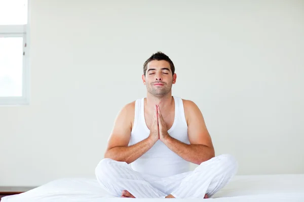 Homem sentado na cama meditando com os olhos fechados — Fotografia de Stock