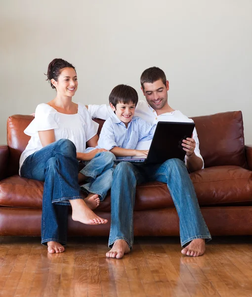 Parents and kid playing with a laptop on a couch — Stock Photo, Image