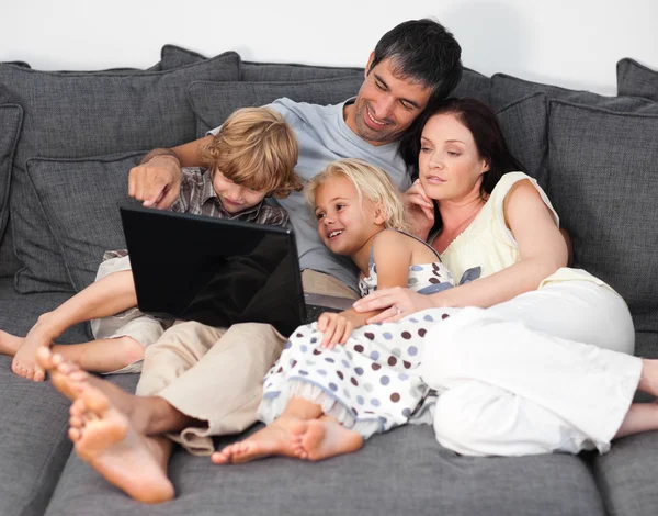 Família encantada usando um laptop em um sofá — Fotografia de Stock