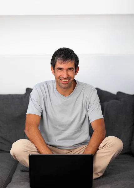 Happy man using a laptop on a grey sofa — Stock Photo, Image