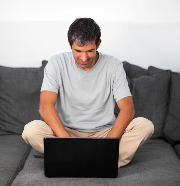 Mutlu bir adam gri kanepede bir dizüstü bilgisayar kullanarak — Stok fotoğraf