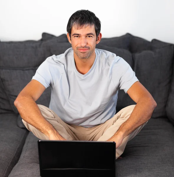 Boldog ember használ egy laptop, egy szürke kanapé — Stock Fotó