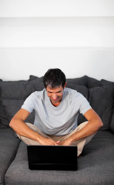 Homem feliz usando um laptop em um sofá cinza — Fotografia de Stock