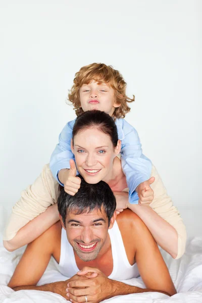 Família brincando na cama com o polegar para cima — Fotografia de Stock