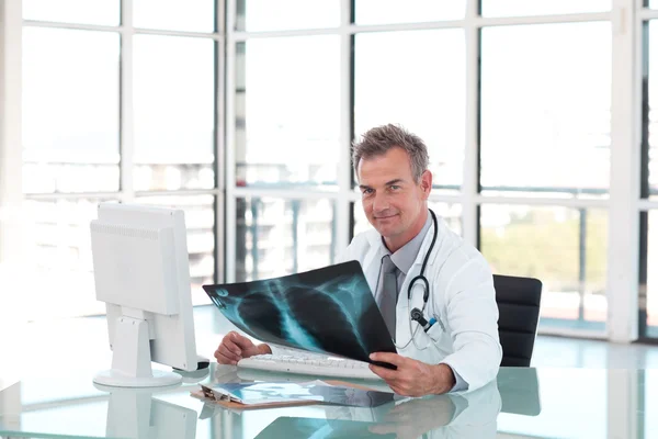 Portrét hansdome lékař zkoumá rentgen u stolu — Stock fotografie