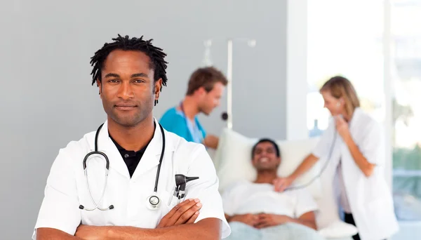 Allvarliga läkare med korslagda armar och patienten i bakgrunden — Stockfoto