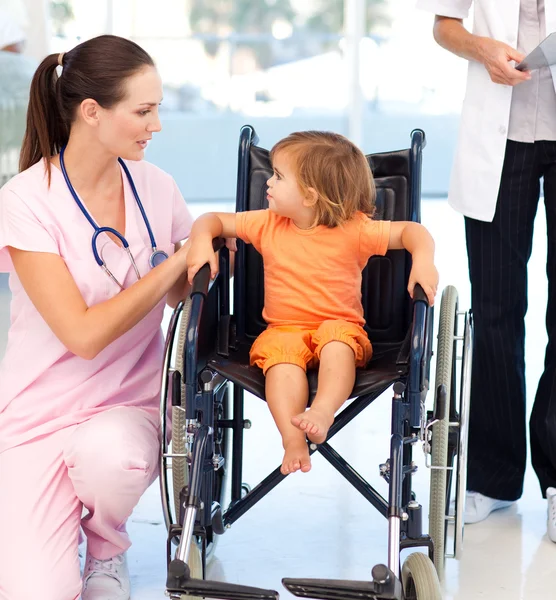 Młoda pielęgniarka mówi do dziecka w wózku inwalidzkim — Zdjęcie stockowe