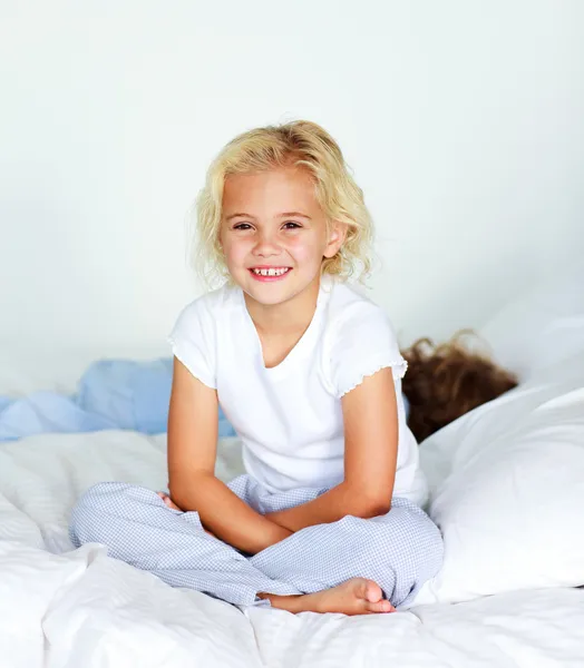 Kleines Mädchen, das auf dem Bett sitzt und in die Kamera lächelt — Stockfoto