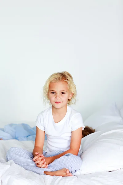 Sorridente ragazza bionda seduta su un letto — Foto Stock