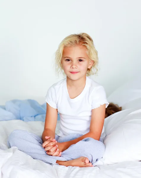 Kleines Mädchen, das auf dem Bett sitzt und in die Kamera schaut — Stockfoto