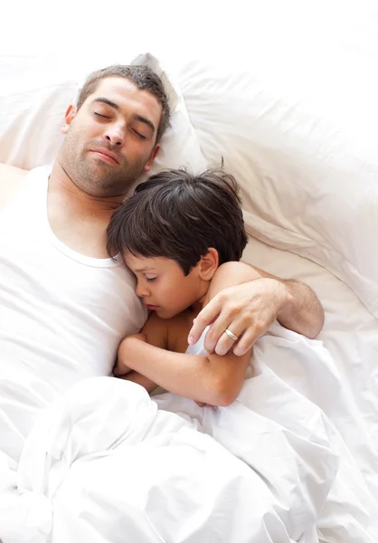 Charmanter Vater und sein Sohn schauen auf dem Bett in die Kamera — Stockfoto