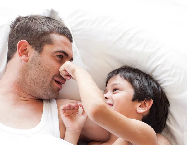 Charming father and his son looking at the camera on the bed — Stock Photo, Image
