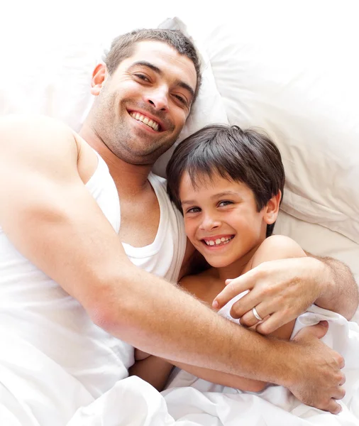 Okouzlující otec a jeho syn při pohledu na fotoaparát na postel — Stock fotografie