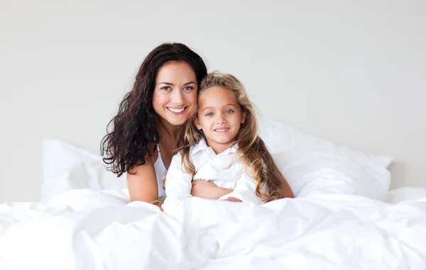 美しい母親と彼女の娘のベッドの上にカメラを見て — ストック写真