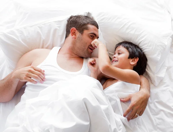 Charmante vader en zijn zoon kijken naar de camera op het bed — Stockfoto