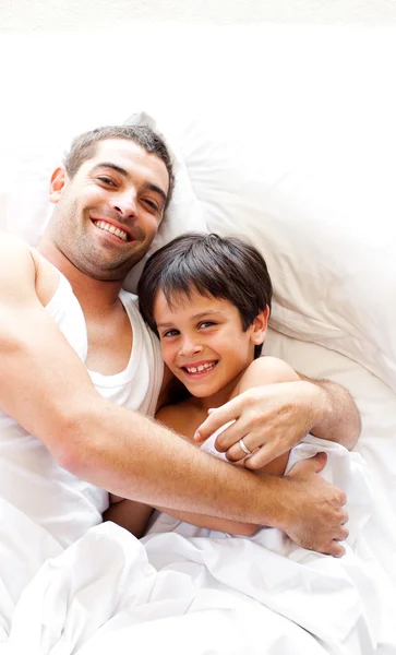 Charming father and his son looking at the camera on the bed — Stock Photo, Image
