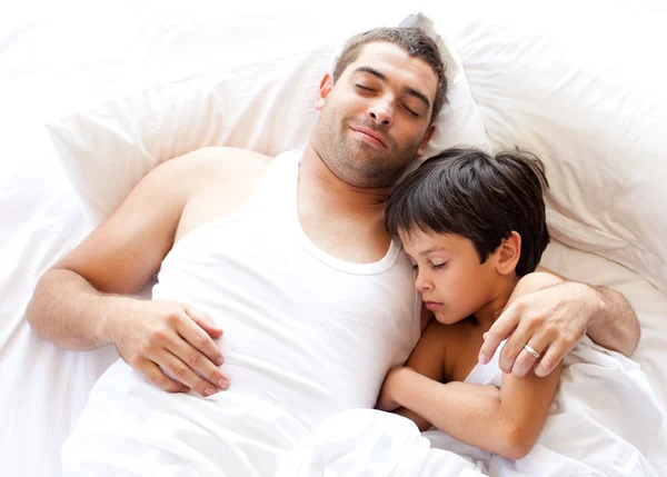 Charmanter Vater und sein Sohn schauen auf dem Bett in die Kamera — Stockfoto