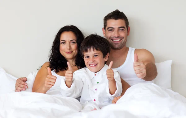 Happy son with thumbs up and his parents in bed — Stock Photo, Image