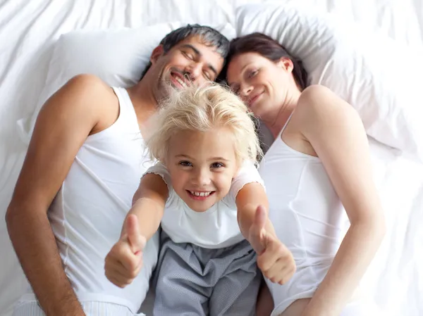 Menina feliz na cama com os polegares para cima e seus pais — Fotografia de Stock