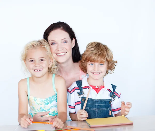 Niños haciendo deberes con su madre sonriendo a la cámara —  Fotos de Stock