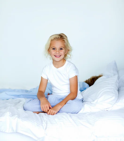 Smiling blonde girl sitting on a bed — Stock Photo, Image