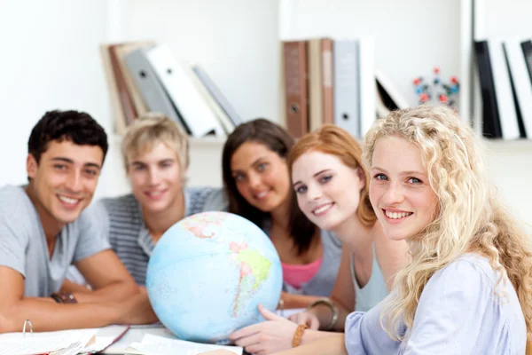 Adolescentes sonrientes en una biblioteca trabajando con un globo terrestre —  Fotos de Stock