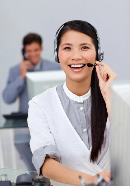 Skrattar asiatiska affärskvinna med headset på en dator — Stockfoto