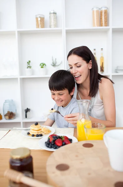 Uśmiechnięty chłopiec jeść placki z matką na śniadanie — Zdjęcie stockowe