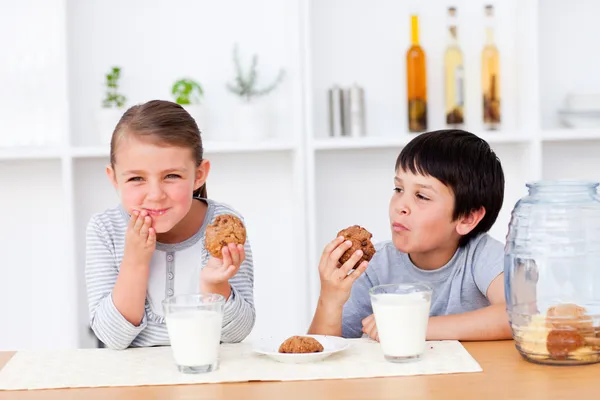 Šťastný sourozenci jíst cukroví a konzumní mléko — Stock fotografie