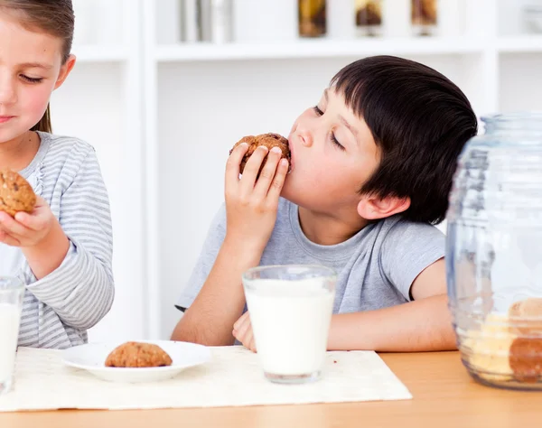 Hermanos sonrientes comiendo galletas y bebiendo leche — Foto de Stock