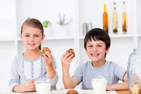 Улыбающиеся брат и сестра едят печенье и пьют молоко — стоковое фото