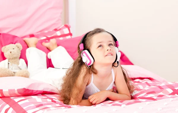 Cute little girl listening music lying on her bed — Stock Photo, Image