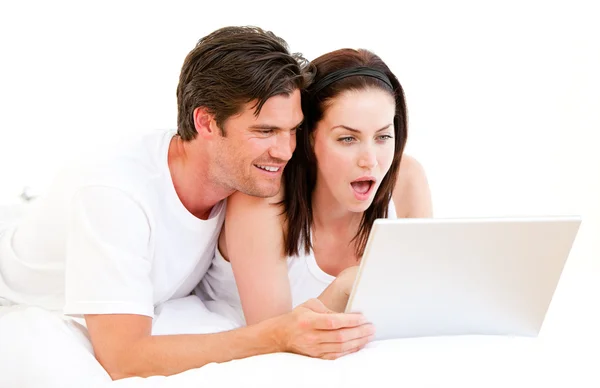 Sürpriz çift onların yatakta yatarken bir bilgisayar kullanarak — Stok fotoğraf