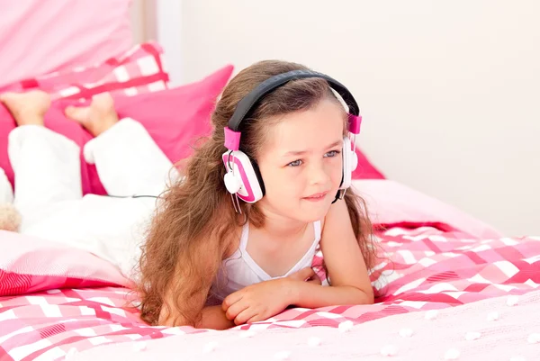 Cheerful little girl listening music lying on her bed — Stock Photo, Image