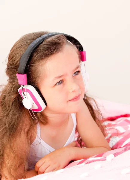 Niña sonriente escuchando música tumbada en su cama —  Fotos de Stock
