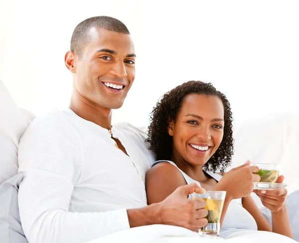Happy couple drinking a cup of tea lying on their bed — Stock Photo, Image