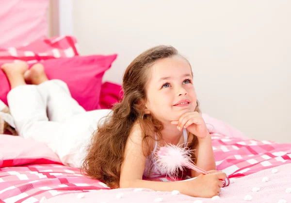 Улыбающаяся маленькая девочка пишет на блокноте, лежащем на ее кровати — стоковое фото