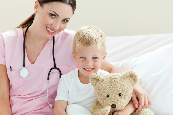 Sorrindo menino segurando um ursinho de pelúcia em uma cama de hospital — Fotografia de Stock