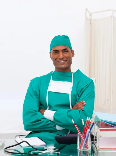 Médico sorridente com os braços dobrados em sua mesa — Fotografia de Stock
