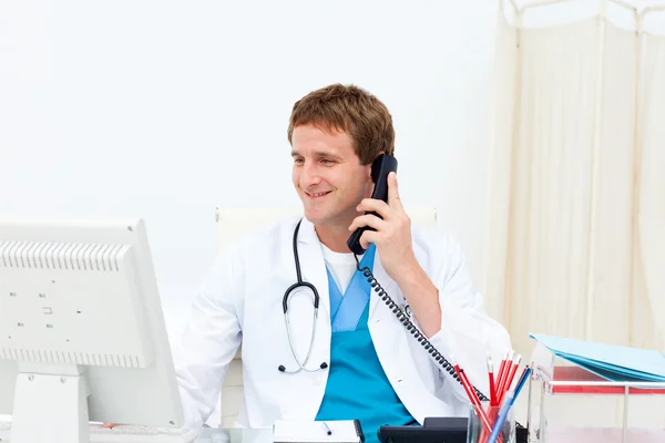 Retrato de um médico sorridente ao telefone em sua mesa — Fotografia de Stock